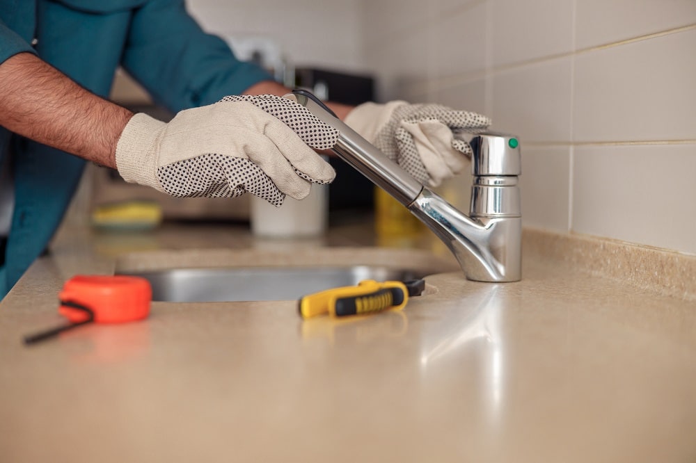 Male plumber repair sink faucet at customer kitchen. Maintenance and household assistance concept