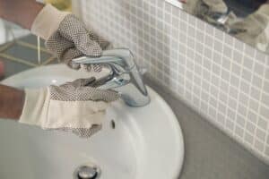 Handyman is repairing faucet of a sink at bathroom. Maintenance and household assistance concept