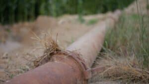 A closeup of a rusty pipe on a blurred green fields background