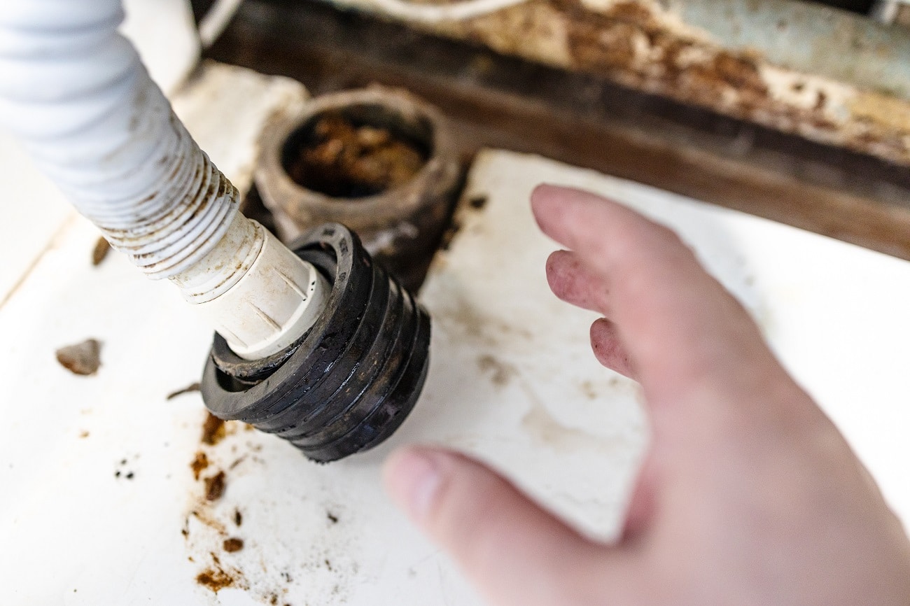 hand of plumber near sewer pipe and corrugated drain hose close up in old village house