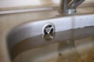 Stainless steel sink plug hole close up full of water and particles of food. Overflowing kitchen sink, clogged drain. Problems with the water supply