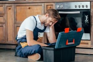 tired young foreman sitting with toolbox near broken oven