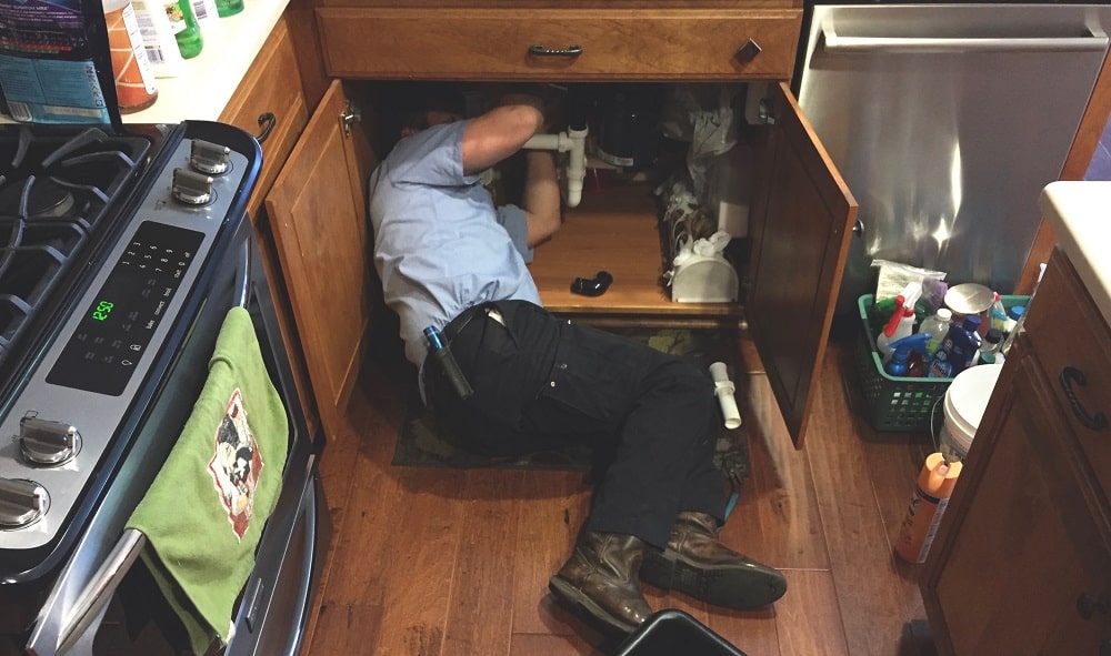 Man working under the kitchen sink fixing the plumbing.