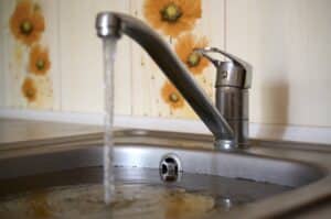 Stainless steel sink plug hole close up full of water and particles of food. Overflowing kitchen sink, clogged drain. Problems with the water supply