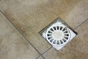 Water drain vent in kitchen, bathroom or basement ceramic tiled old vintage floor. Geometric abstract beige background.